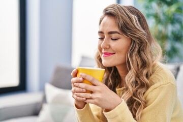 Young woman drinking coffee sitting on sofa at home