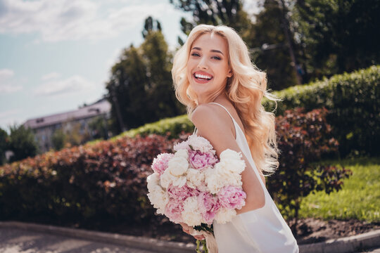 Photo of funky sweet young wavy woman wear white top walking holding flowers enjoying sunshine outside city park