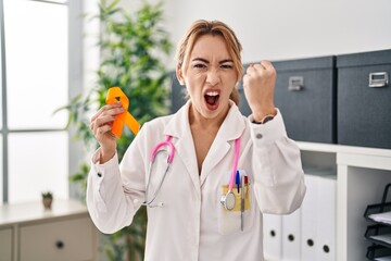 Hispanic doctor woman holding awareness orange ribbon annoyed and frustrated shouting with anger,...