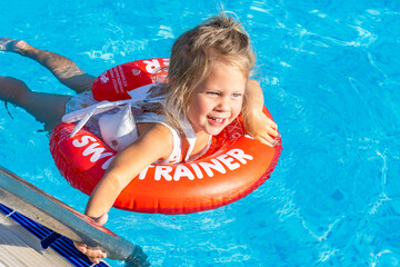 Joyful laughing white caucasian girl 2 years old with blond hair on a red inflatable ring while...