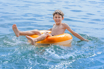 A boy of 9 years old has fun riding a swimming ring while swimming in the sea