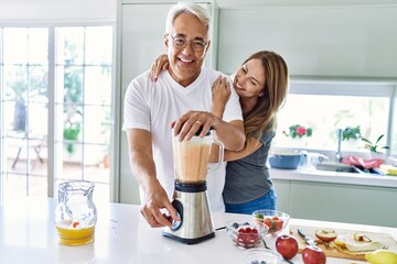 Middle age hispanic couple smiling happy and hugging cooking smoothie at the kitchen.