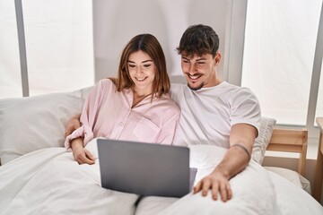 Mand and woman couple using laptop sitting on bed at bedroom