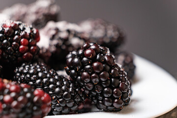 Blackberries sprinkled with sugar in a plate on a black background, close-up view from the side.