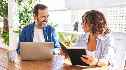 Middle age hispanic couple reading book and using laptop at terrace