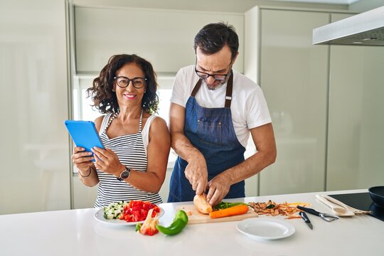 Middle age hispanic couple smiling confident cooking and using touchpad at kitchen