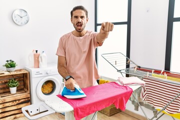 Young hispanic man ironing clothes at home pointing displeased and frustrated to the camera, angry and furious with you