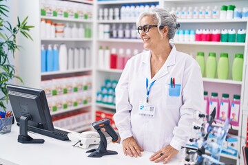 Middle age grey-haired woman pharmacist smiling confident standing at pharmacy