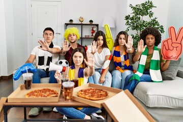 Group of young people wearing team scarf cheering football game with open hand doing stop sign with serious and confident expression, defense gesture
