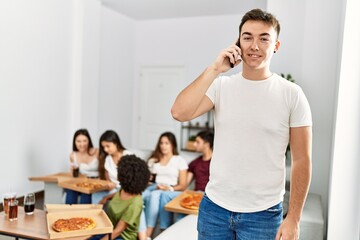 Group of young friends eating italian sitting on the sofa. Man smiling and talking on the smartphone at home.