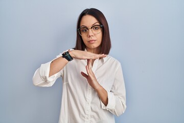 Young hispanic woman standing over white background doing time out gesture with hands, frustrated...