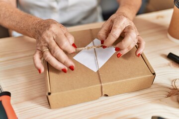 Senior grey-haired woman business worker preparing package order at office