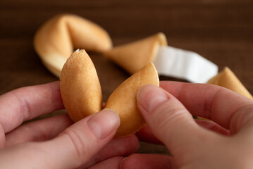 Person holding in hand fortune cookie against few cookies laying on table surface background