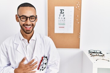 Fototapeta na wymiar African american optician man standing by eyesight test smiling and laughing hard out loud because funny crazy joke with hands on body.
