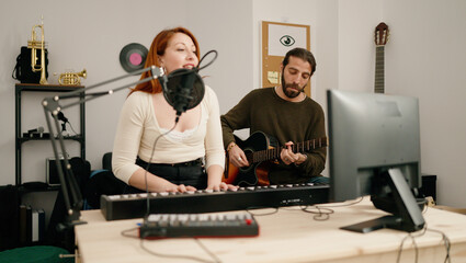 Man and woman singing son playing guitar and keyboard piano at music studio