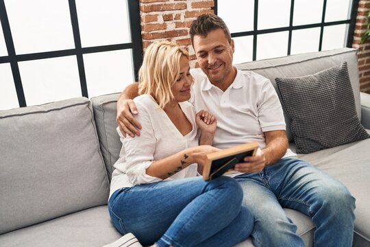Middle age man and woman hugging each other looking photo at home
