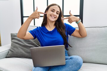 Young brunette woman using laptop at home smiling cheerful showing and pointing with fingers teeth and mouth. dental health concept.