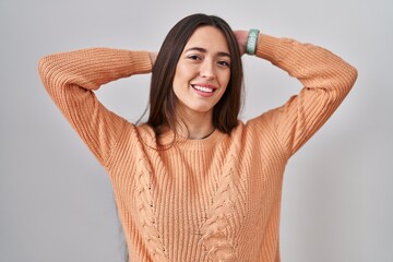 Fototapeta na wymiar Young brunette woman standing over white background relaxing and stretching, arms and hands behind head and neck smiling happy