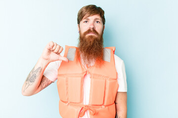 Young caucasian man wearing life jacket isolated on blue background showing a dislike gesture,...