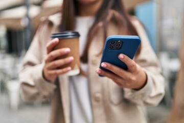 Young hispanic woman using smartphone drinking coffee at street