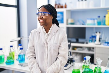 African american woman working at scientist laboratory looking to side, relax profile pose with...