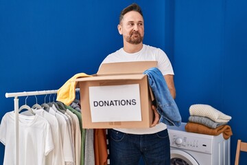 Middle age caucasian man holding donations box smiling looking to the side and staring away...