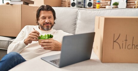 Middle age man using laptop eating salad at new home