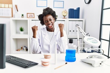 African dentist woman working at medical clinic very happy and excited doing winner gesture with arms raised, smiling and screaming for success. celebration concept.
