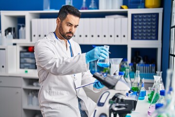 Young hispanic man scientist holding measuring liquid at laboratory