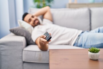 Young hispanic man lying on sofa watching movie at home
