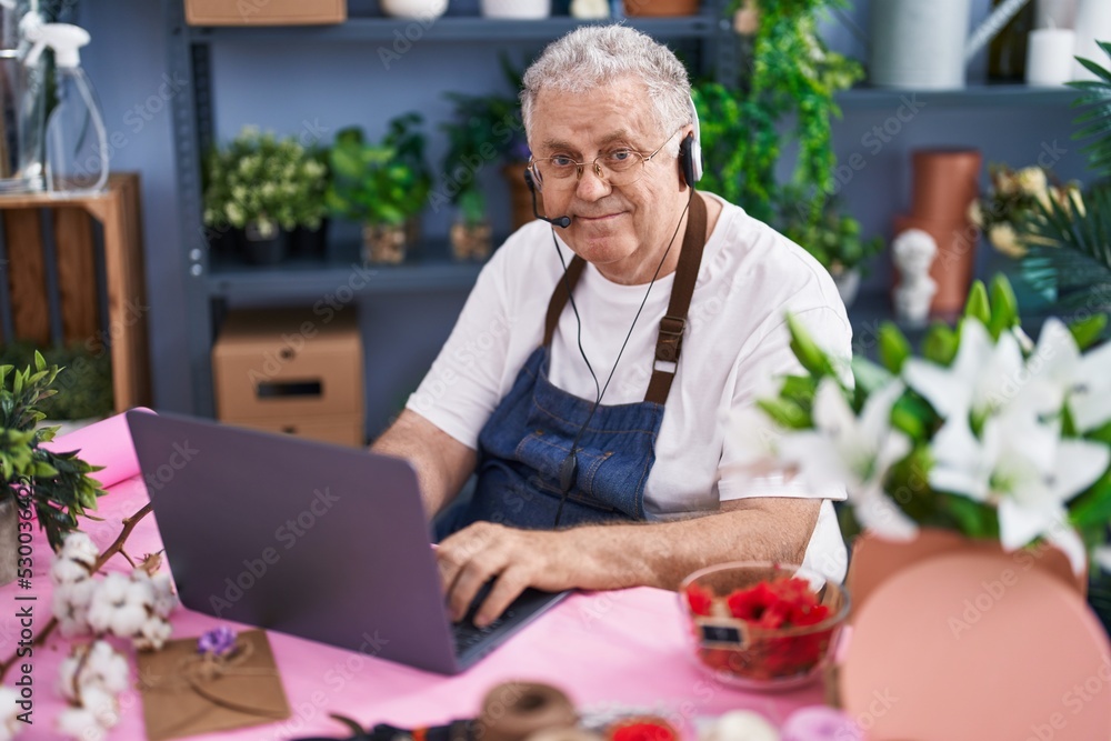 Poster middle age grey-haired man florist using laptop and headphones at florist