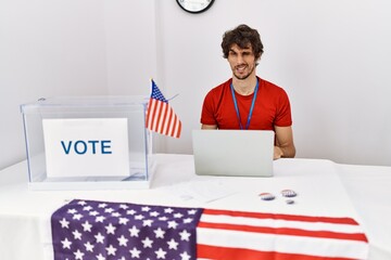 Young hispanic man at political election sitting by ballot winking looking at the camera with sexy...