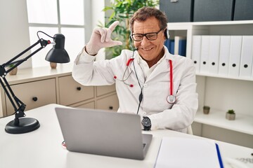 Obraz premium Senior doctor man working on online appointment smiling and confident gesturing with hand doing small size sign with fingers looking and the camera. measure concept.