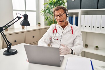 Obraz premium Senior doctor man working on online appointment in shock face, looking skeptical and sarcastic, surprised with open mouth