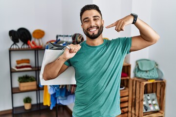 Young handsome man with beard holding shopping bags at retail shop smiling cheerful showing and pointing with fingers teeth and mouth. dental health concept.