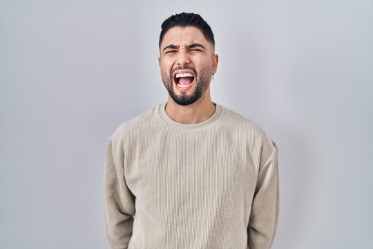 Young handsome man standing over isolated background angry and mad screaming frustrated and furious, shouting with anger. rage and aggressive concept.