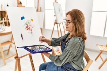 Fototapeta na wymiar Middle age artist woman smiling happy painting at art studio