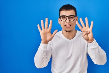 Young arab man wearing casual white shirt and glasses showing and pointing up with fingers number...