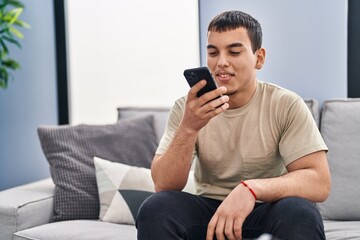 Young man using smartphone sitting on sofa at home