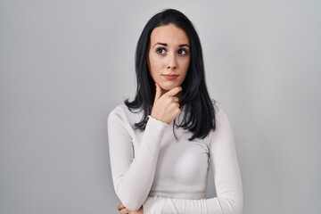 Fototapeta premium Hispanic woman standing over isolated background looking confident at the camera with smile with crossed arms and hand raised on chin. thinking positive.