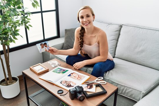 Young caucasian woman making photo book sitting on sofa at home
