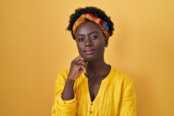 African young woman wearing african turban with hand on chin thinking about question, pensive expression. smiling with thoughtful face. doubt concept.