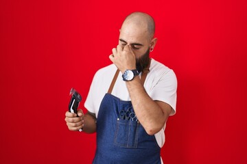 Young hispanic man with beard and tattoos wearing barber apron holding razor tired rubbing nose and...