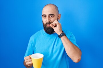 Young hispanic man with beard and tattoos drinking a cup of coffee mouth and lips shut as zip with...