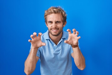 Caucasian man standing over blue background smiling funny doing claw gesture as cat, aggressive and sexy expression