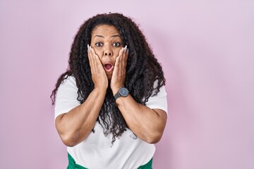 Plus size hispanic woman standing over pink background afraid and shocked, surprise and amazed...