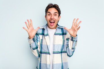 Naklejka premium Young hispanic man isolated on blue background celebrating a victory or success, he is surprised and shocked.