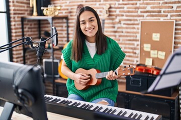 Young hispanic woman musician playing ukulele at music studio
