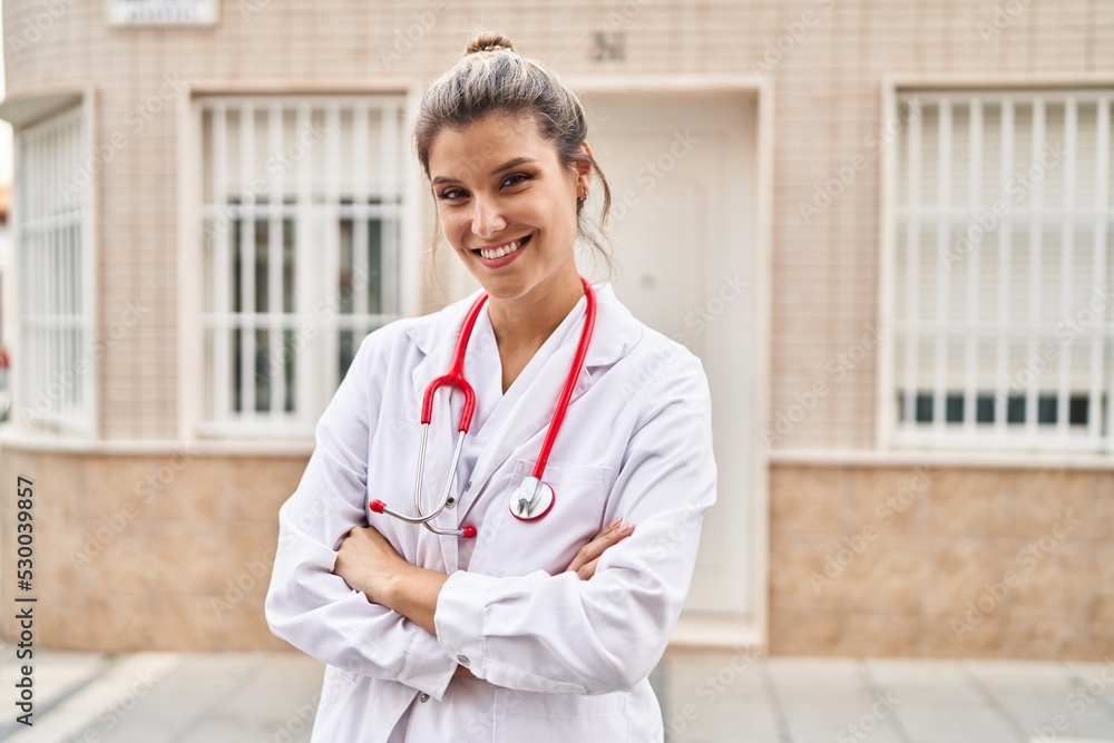 Poster young blonde woman wearing doctor uniform standing with arms crossed gesture at street