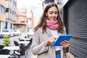 Young beautiful hispanic woman using touchpad wearing scarf at street